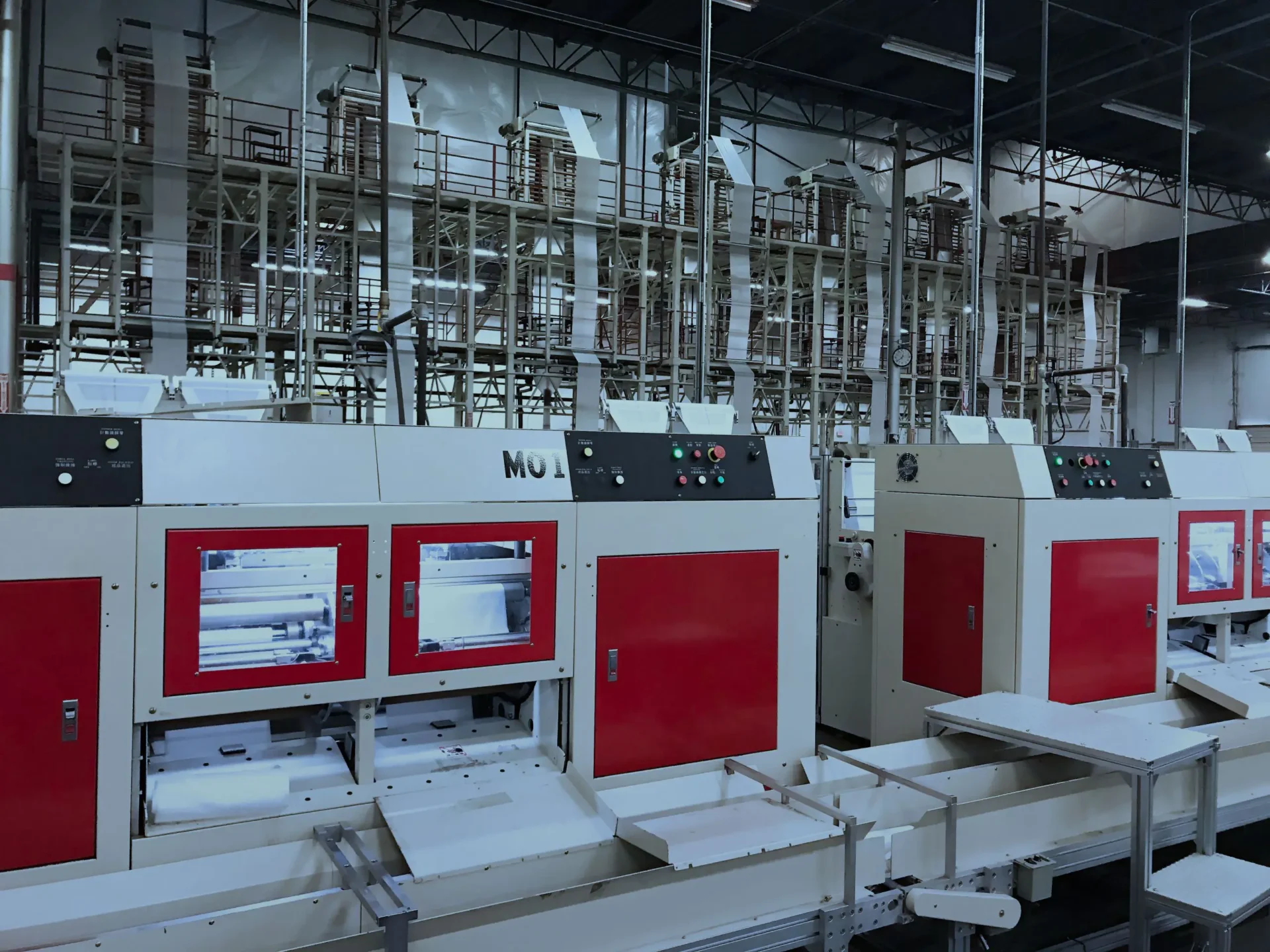 Warehouse1-scaled Rows of large white and red industrial machines in a factory setting with extensive piping and metal structures in the background.