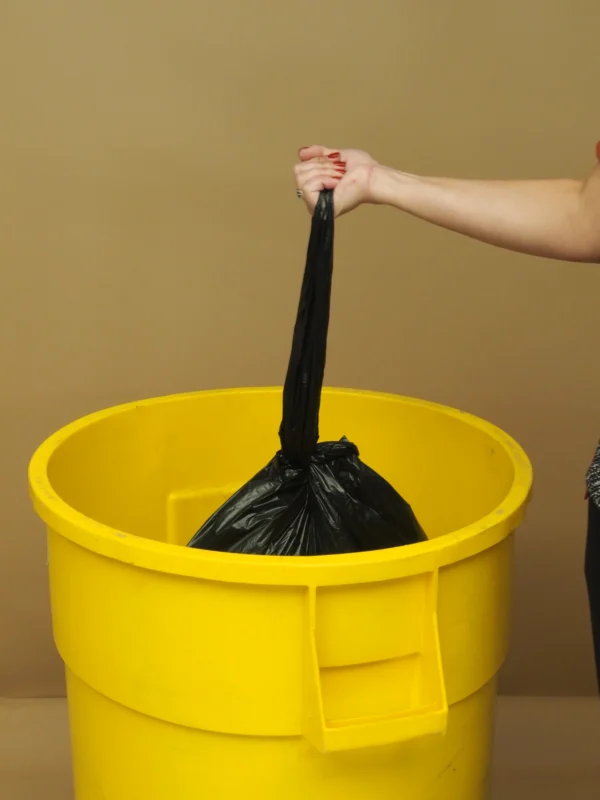 A person is putting trash bags in a yellow bucket.